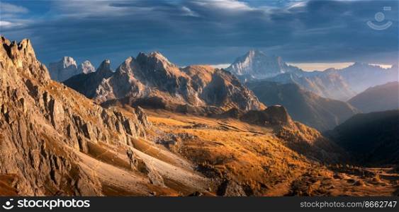 Beautiful mountains at sunset in autumn. Nature in Dolomites, Italy. Colorful panoramic landscape with rocks, orange grass and trees on hills, trail, dirt road, stones, blue sky with clouds in fall