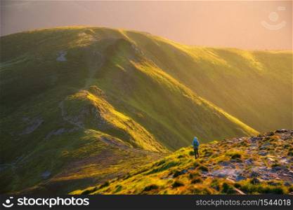 Beautiful mountains in fog and standing woman with backpack on the mountain peak at sunset in summer. Landscape with girl on the trail, stones, green hills lighted by sunbeams. Travel and tourism