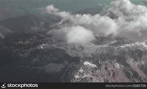 Beautiful mountains landscape with clouds over the tops, view from flying airplane