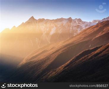 Beautiful mountains with snowy peaks at sunny morning in Nepal. Silhouettes of Himalayan mountains at sunrise. Colorful landscape with high rocks, blue sky and gold sunbeam. Amazing Himalayas. Nature
