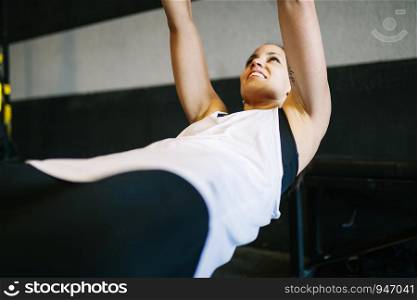 Beautiful muscular woman doing exercise with trx system. Young woman exercising with suspension trainer at gym.