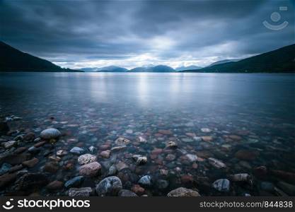 Beautiful mystic landscape lake scenery in Scotland with cloudy sky and sunbeams