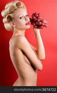 Beautiful naked blond woman over red background with some red grape