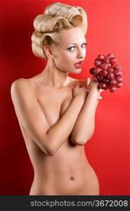 Beautiful naked blond woman over red background with some red grape looking in camera