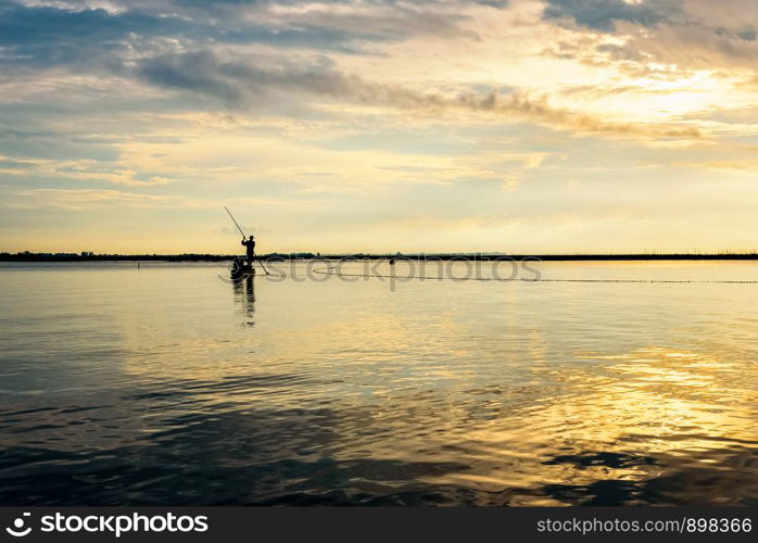 Beautiful nature landscape, bright golden sunlight in the sky and silhouette fisherman on a small boat use fishing nets in the morning during the sunrise over Songkhla Lake, Phatthalung, Thailand. Fisherman on the boat use fishing nets at sunrise, Thailand