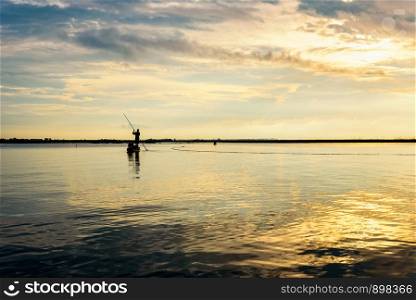 Beautiful nature landscape, bright golden sunlight in the sky and silhouette fisherman on a small boat use fishing nets in the morning during the sunrise over Songkhla Lake, Phatthalung, Thailand. Fisherman on the boat use fishing nets at sunrise, Thailand