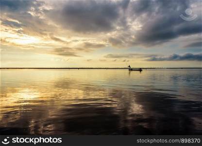 Beautiful nature landscape, bright golden sunlight in the sky and silhouette fisherman on a small boat use fishing nets in the morning during the sunrise over Songkhla Lake, Phatthalung, Thailand. Fisherman on the boat use fishing nets at sunrise, Thailand