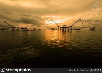 Beautiful nature landscape colorful golden light of the morning sky at sunrise and native fishing tool rural lifestyle at Pakpra canal, Songkhla Lake, Baan Pak Pra, landmark of Phatthalung, Thailand. Golden light in the sky at sunrise and native fishing tool, Thailand