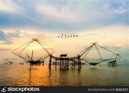 Beautiful nature landscape golden light of the morning sky at sunrise with flock of birds are flying over the native fishing tool, rural lifestyle at Pakpra canal, Baan Pak Pra, Phatthalung, Thailand. Rural lifestyle at Pakpra canal during sunrise in Thailand