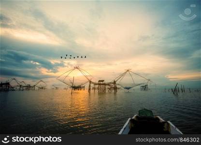 Beautiful nature landscape golden light of the morning sky at sunrise with flock of birds are flying, native fishing tool and prow, rural lifestyle at Pakpra canal, Baan Pak Pra, Phatthalung, Thailand. Rural lifestyle at Pakpra canal during sunrise in Thailand