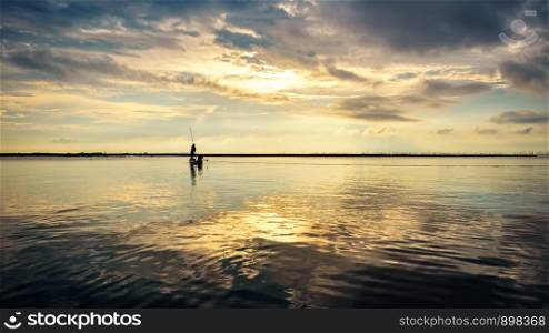 Beautiful nature landscape golden sunlight in the sky and silhouette fisherman on a small boat use fishing nets in the morning at sunrise over Songkhla Lake, Phatthalung, Thailand, 16:9 widescreen. Fisherman on the boat use fishing nets at sunrise, Thailand
