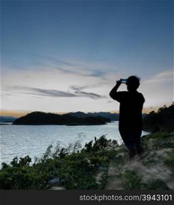 Beautiful nature landscape of mountain with lake, silhouette man take photo with smart phone. Kaeng Krachan Reservoir in Thailand