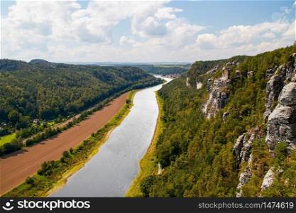 beautiful nature panorama of the river valley landscape of the Elbe in the Elbe Sandstone Mountains of Saxon Switzerland near Dresden with green forests and under a blue sky. Panorama of the river valley of the Elbe in the Elbe Sandstone Mountains of Saxon Switzerland