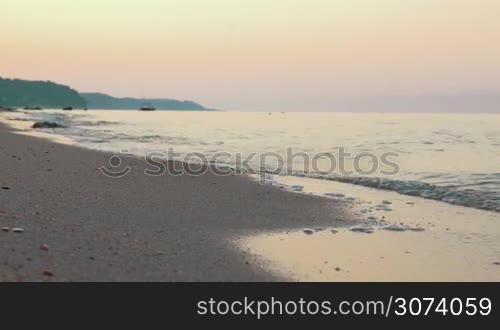 Beautiful nature scene. Quiet sea waves washing the shore at sunset. Clear sky in warm evening colors
