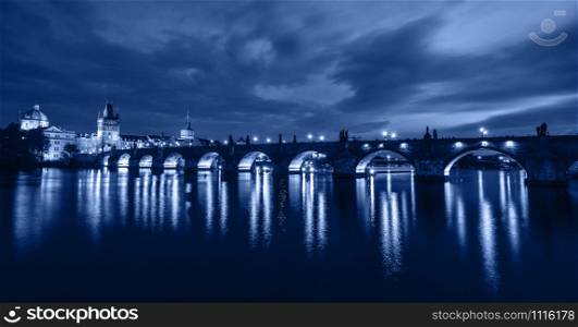 Beautiful night view of Charles Bridge and Vltava river, Prague, Czech Republic. Charles Bridge and Vltava river with night lights. Trendy banner toned in classic blue - color of the 2020 year. Beautiful night view of Charles Bridge and Vltava river, Prague, Czech Republic.