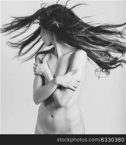 Beautiful nude woman with moving hair on white background. Black and white studio photograph.
