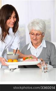 Beautiful nurse bringing meal tray to old woman at nursing home