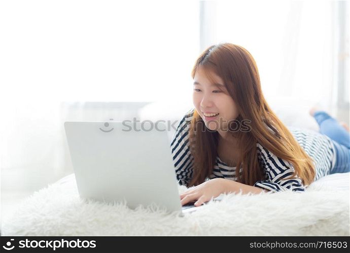 Beautiful of portrait asian young woman lying on bed using laptop at bedroom for leisure and relax, freelance with girl working notebook, communication concept.