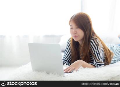 Beautiful of portrait asian young woman lying on bed using laptop at bedroom for leisure and relax, freelance with girl working notebook, communication concept.