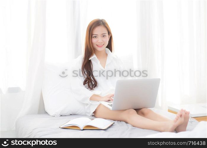 Beautiful of portrait asian young woman setting on bed using laptop computer and notebook at bedroom for leisure and relax, freelance with girl working at bedroom with note, communication and lifestyle concept.