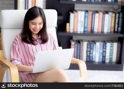 Beautiful of portrait asian young woman working online laptop sitting on chair at living room, girl using notebook computer with connect to internet for distance job, business and success concept.