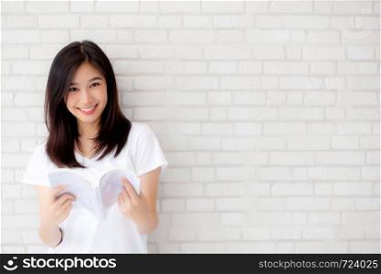 Beautiful of portrait young asian woman happiness relax standing reading book on concrete cement white background at home, girl happy study content literature, education and lifestyle concept.