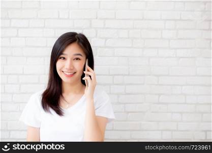 Beautiful of portrait young asian woman talk smart phone and smile standing on cement brick background, freelance female calling telephone, communication of mobile concept.