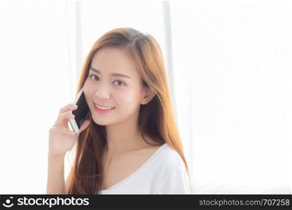 Beautiful of portrait young asian woman talking smart mobile phone and smile standing at curtain background on bedroom, girl calling telephone, communication concept.