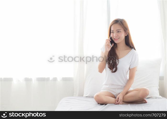 Beautiful of portrait young asian woman talking smart mobile phone and smile sitting at curtain background on bedroom, girl calling telephone, communication concept.