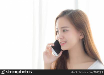 Beautiful of portrait young asian woman talking smart mobile phone and smile standing at curtain background on bedroom, girl calling telephone, communication concept.
