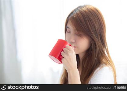 Beautiful of portrait young asian woman with drink acup of coffee standing curtain window background in bedroom, girl relax in morning at home, lifestyle concept.