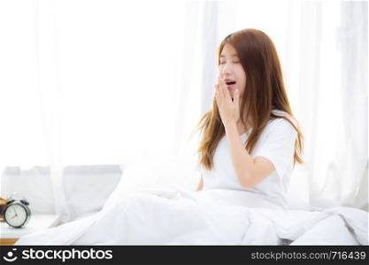 Beautiful of portrait young asian woman yawn sitting with sleep on bed at bedroom, girl wake up after resting and leisure with wellness, lifestyle concept.