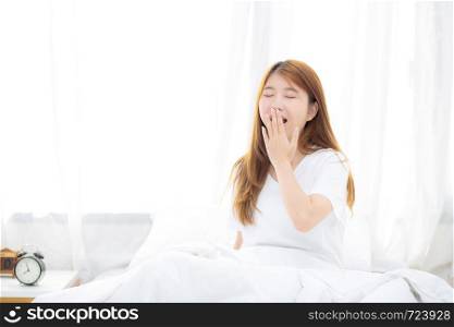 Beautiful of portrait young asian woman yawn sitting with sleep on bed at bedroom, girl wake up after resting and leisure with wellness, lifestyle concept.