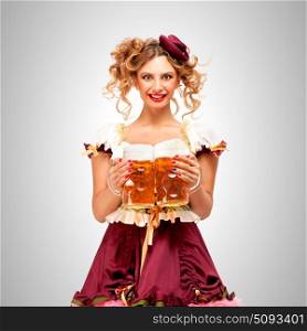 Beautiful Oktoberfest waitress wearing a traditional Bavarian dress dirndl, holding beer mugs on grey background.