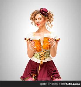Beautiful Oktoberfest waitress wearing a traditional Bavarian dress dirndl, holding beer mugs on grey background.