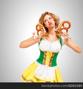 Beautiful Oktoberfest woman wearing a traditional Bavarian dress dirndl holding pretzels, on grey background.