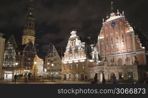 Beautiful old architecture of the central square of Riga. Night view with illuminated buildings and people silhouettes.