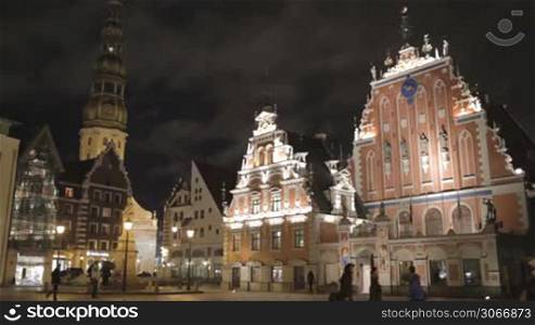 Beautiful old architecture of the central square of Riga. Night view with illuminated buildings and people silhouettes.