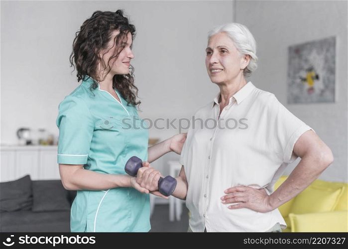 beautiful old lady is doing exercise with dumbbell with help physiotherapist