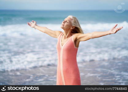 Beautiful older female spreading her arms on a beautiful beach, spending her leisure time. Elderly woman enjoying her retirement at a seaside retreat.. Beautiful older female spreading her arms on a beautiful beach, spending her leisure time.