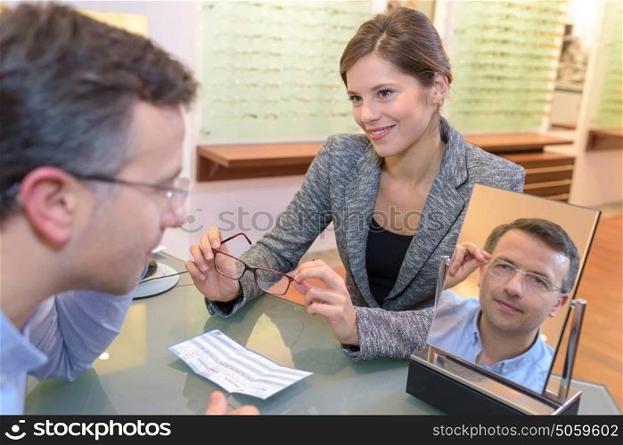 beautiful optician helping male customer choosing eye glasses