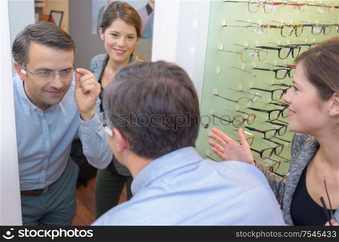 beautiful optician helping male customer choosing eye glasses