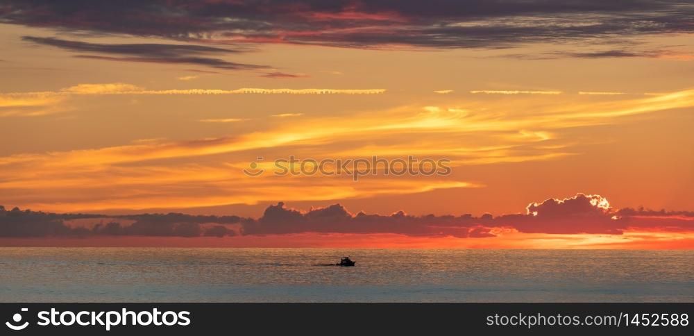 Beautiful orange-and-yellow sunset with a tiny boat sailing off the coast of Cozumel island in Mexico