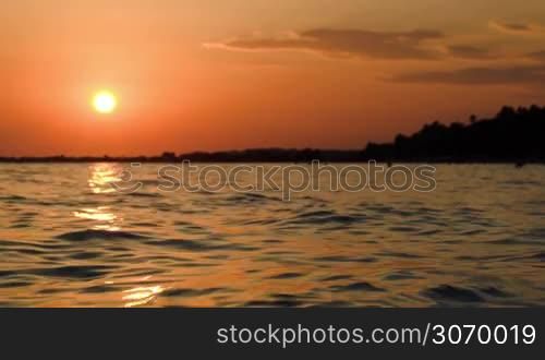 Beautiful orange sunset over dark wavy sea, sun reflecting in water