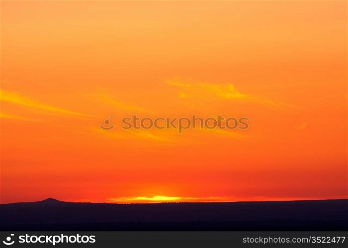 Beautiful orange sunset with the silhouette of a small mountain