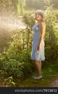 Beautiful outdoor shot of happy woman watering garden bed at sunny day