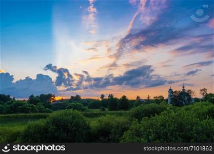Beautiful panorama of bright clouds in the rays of the setting sun and the white church with a bell tower, Russia.