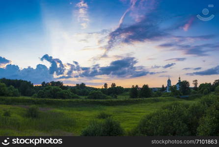 Beautiful panorama of bright clouds in the rays of the setting sun and the white church with a bell tower, Russia.