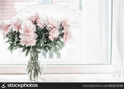 Beautiful pastel pink bouquet of peonies in glass vase on windowsill. Flowers in interior design. Cozy home.