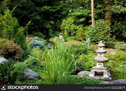 Beautiful peaceful Japanese zen garden used for meditation and relaxation, filled with green vegetation and granite Rokkaku Yukimi Lanterns.